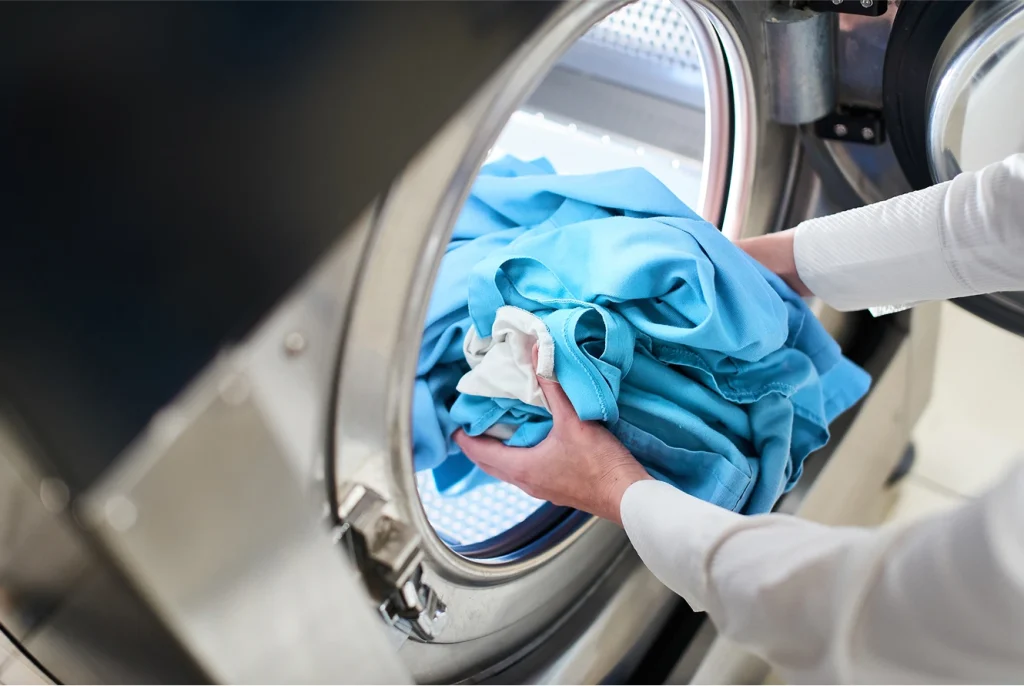 A person loads blue clothes into a front-load washer, showing the convenience of self-service laundry in Arizona.