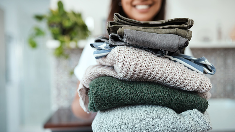 Stacked and ready to be packed. Closeup shot of a young woman holding a pile of folded laundry at home.
