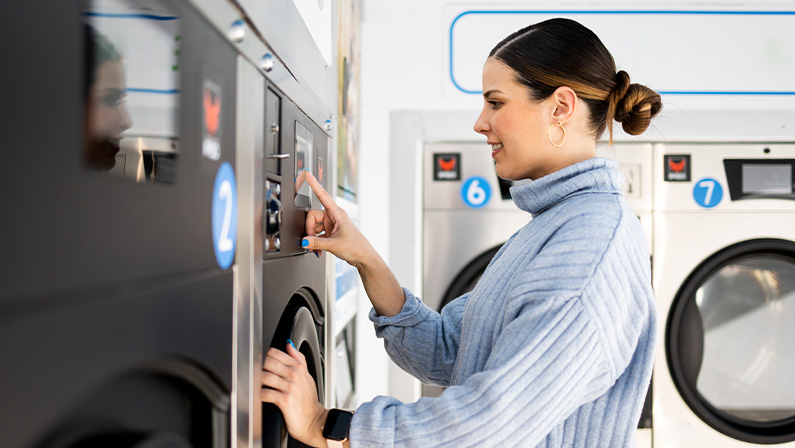 A girl is inside a self-service laundry choosing the washing program.