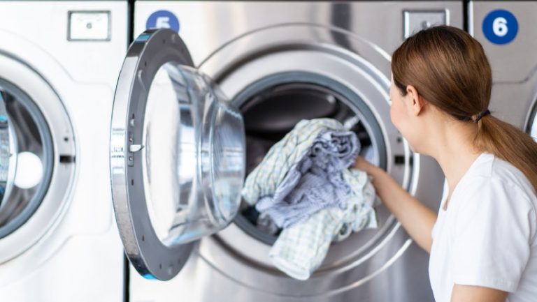 Happy Asian beautiful woman using a self service washing machine KIOSK or automatic washing machine vendor. Woman interacting with a self-service laundry machine at convenience store.