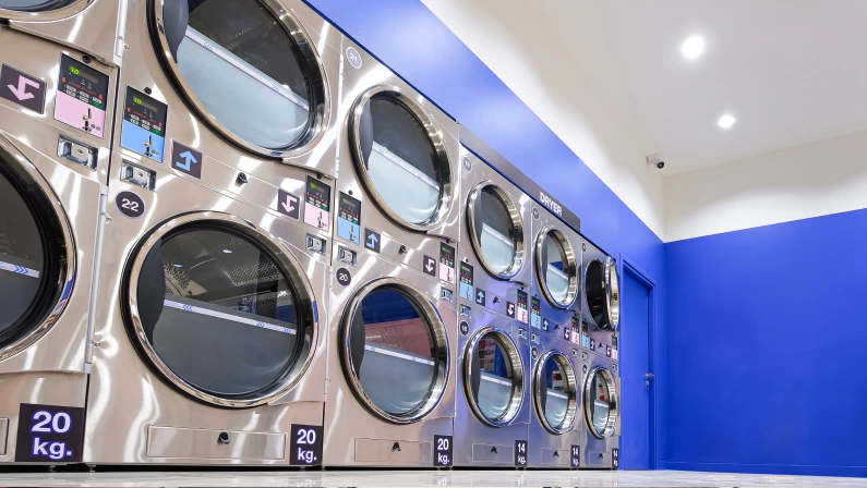 Row of vending washing machines and clothes dryers inside of modern Laundromat Shop
