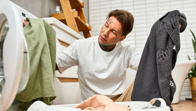 A young man with tattoos sorts clothes as he prepares to do laundry in his comfy home.