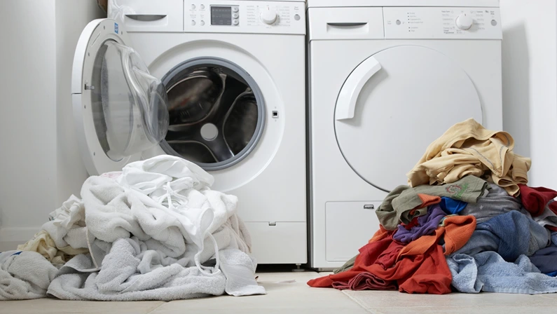 Modern laundry room with a washing machine and dryer, featuring sorted piles of colorful and white clothes ready for cleaning.