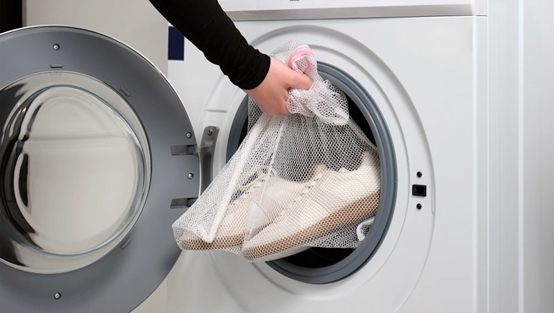 A women holds sports shoes in a laundry bag in a washing machine