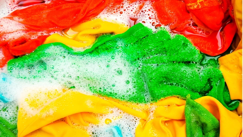 Colored clothes soaked in water with detergent and foam bubbles.