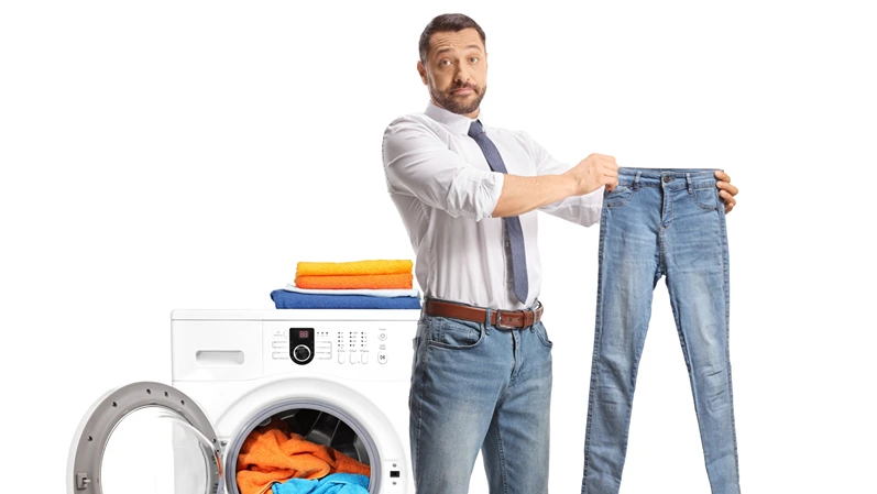 Man standing in front of a washing machine and holding a small pair of jeans