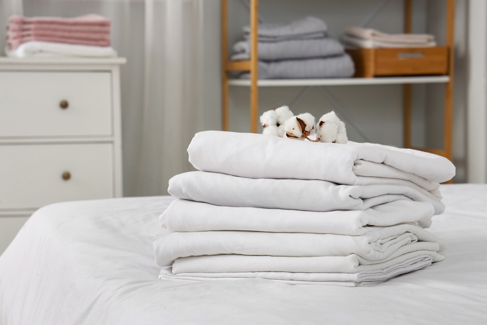 Stack of white linen with cotton flowers on bed in room